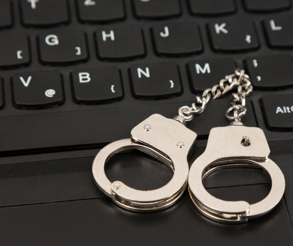 A pair of silver handcuffs placed on a black keyboard, symbolizing the concept of cybercrime and the enforcement of laws related to online criminal activities